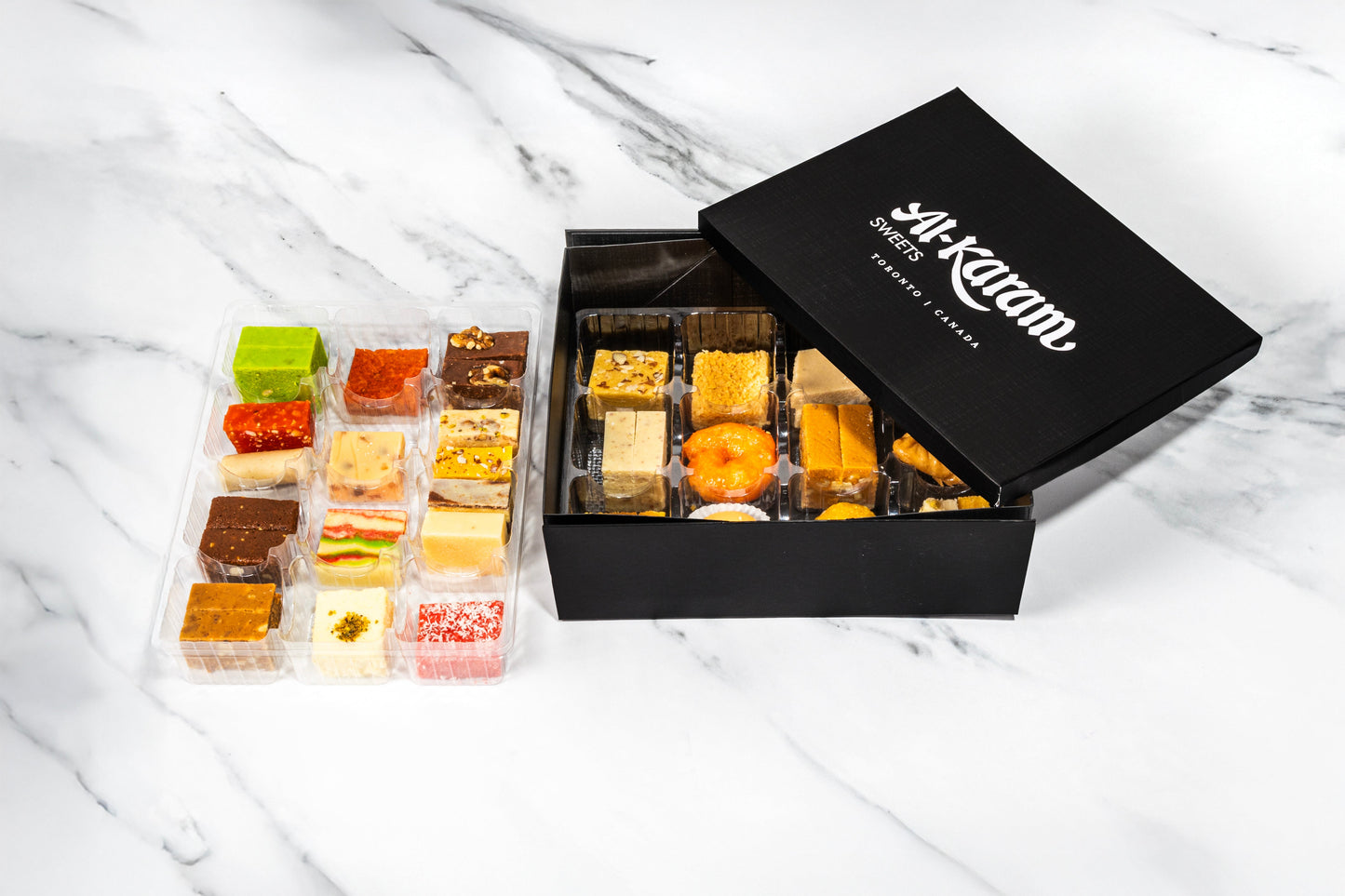 Assorted pastries in a black box on a marble surface with 'Al-Karam Sweets' branding.